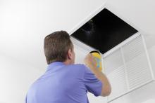 Man inspecting air duct with flashlight