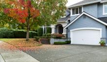 suburban home with fallen red and orange leaves on lawn from tree