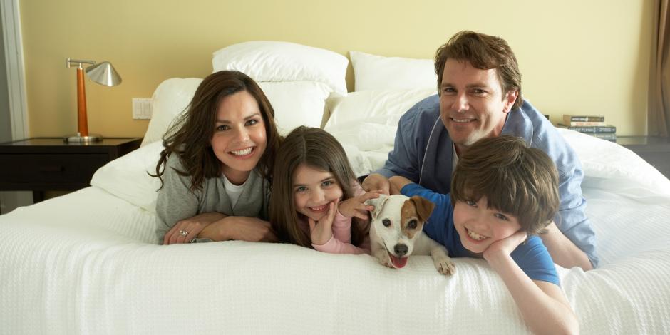 A family of four with a dog laying on a bed