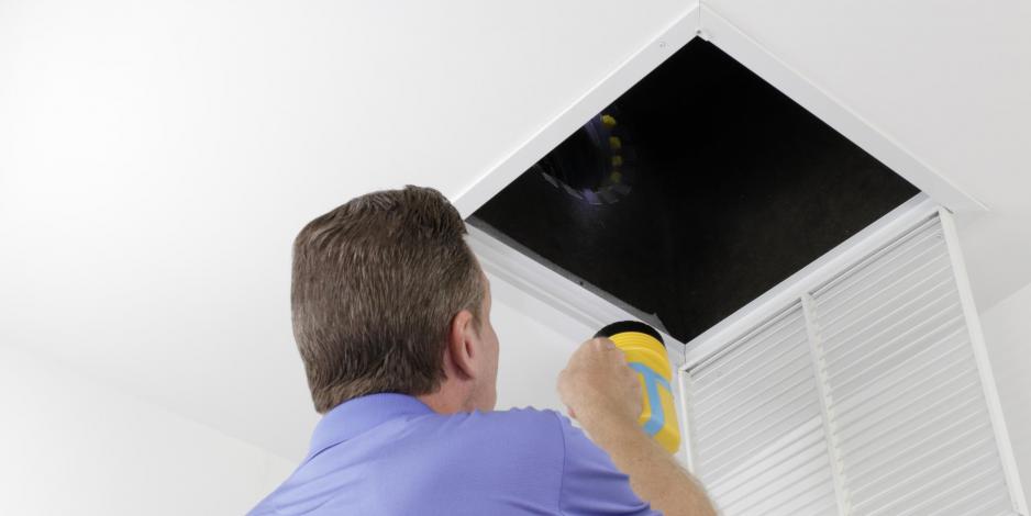 Man inspecting air duct with flashlight